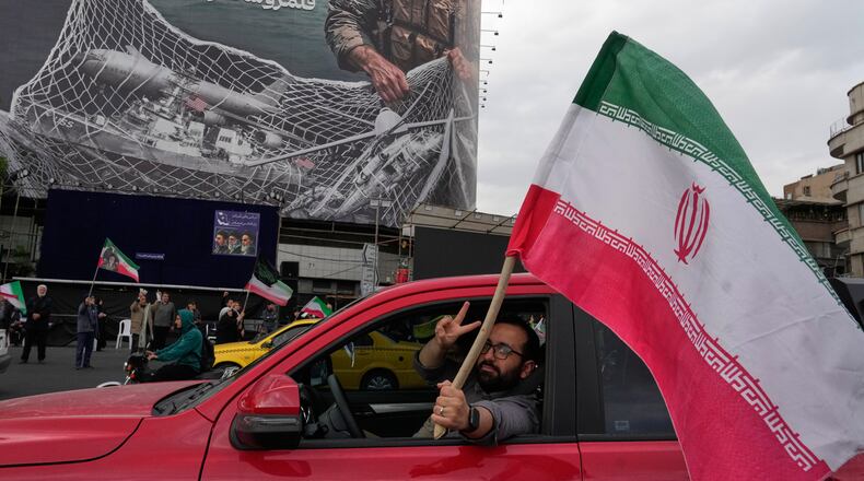 A man flashes a victory sign as he carries an Iranian flag in front of an anti-U.S. billboard depicting the American aircrafts into the Iranian armed forces fishing net with signs that read in Farsi: "The Strait of Hormuz will remain closed, The entire Persian Gulf is our hunting ground," at the Eqelab-e-Eslami, or Islamic Revolution Square in downtown Tehran, Iran, Monday, April 13, 2026. (AP Photo/Vahid Salemi)