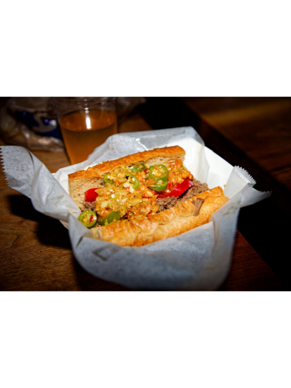 A paper carry-out boat lined with paper contains a buttery, toasted baguette filled with meat, melted cheese and jalapeno peppers.