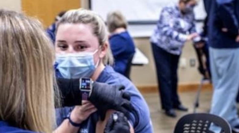 Here, a Wellstar Health System nurse receives a COVID-19 vaccine shot more than a year ago, in December 2020.  Wellstar is among the metro Atlanta health systems mandating that all staff be vaccinated by October 1, and some of its workers have protested.  The nurse in this photo was ICU nurse Amanda Earley, the system's first employee to receive the vaccine.  Wellstar Health System CEO Candice Saunders watched in the foreground as she got the shot. (Photo courtesy of Wellstar)