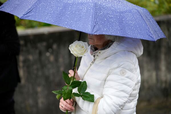 A woman waits under an umbrella to lay a rose during a memorial ceremony in the schoolyard of the Joseph-Koenig high school in Haltern, Germany, ten years after 16 pupils and two teachers of the school died in the Germanwings crash in the French Alps, Monday, March 24, 2025. (AP Photo/Martin Meissner)