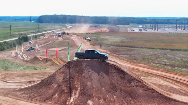 A Rivian pickup truck climbs a dirt mound during a demonstration after the September groundbreaking ceremony at the site of Rivian's future plant in Walton and Morgan counties. (Miguel Martinez/AJC)