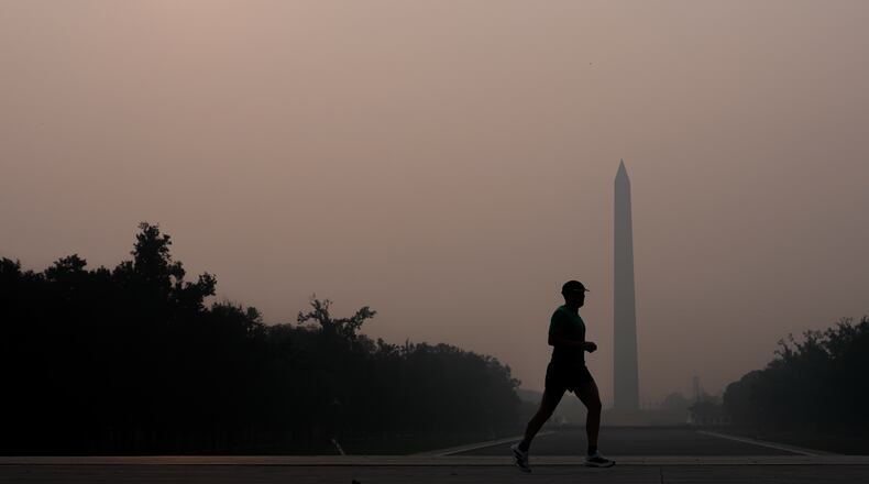 The sun is obscured by wildfire smoke as a person runs in front of the Washington Monument and Lincoln Memorial Reflecting Pool, Friday, July 17, 2026, on the National Mall in Washington. (AP Photo/Julia Demaree Nikhinson)