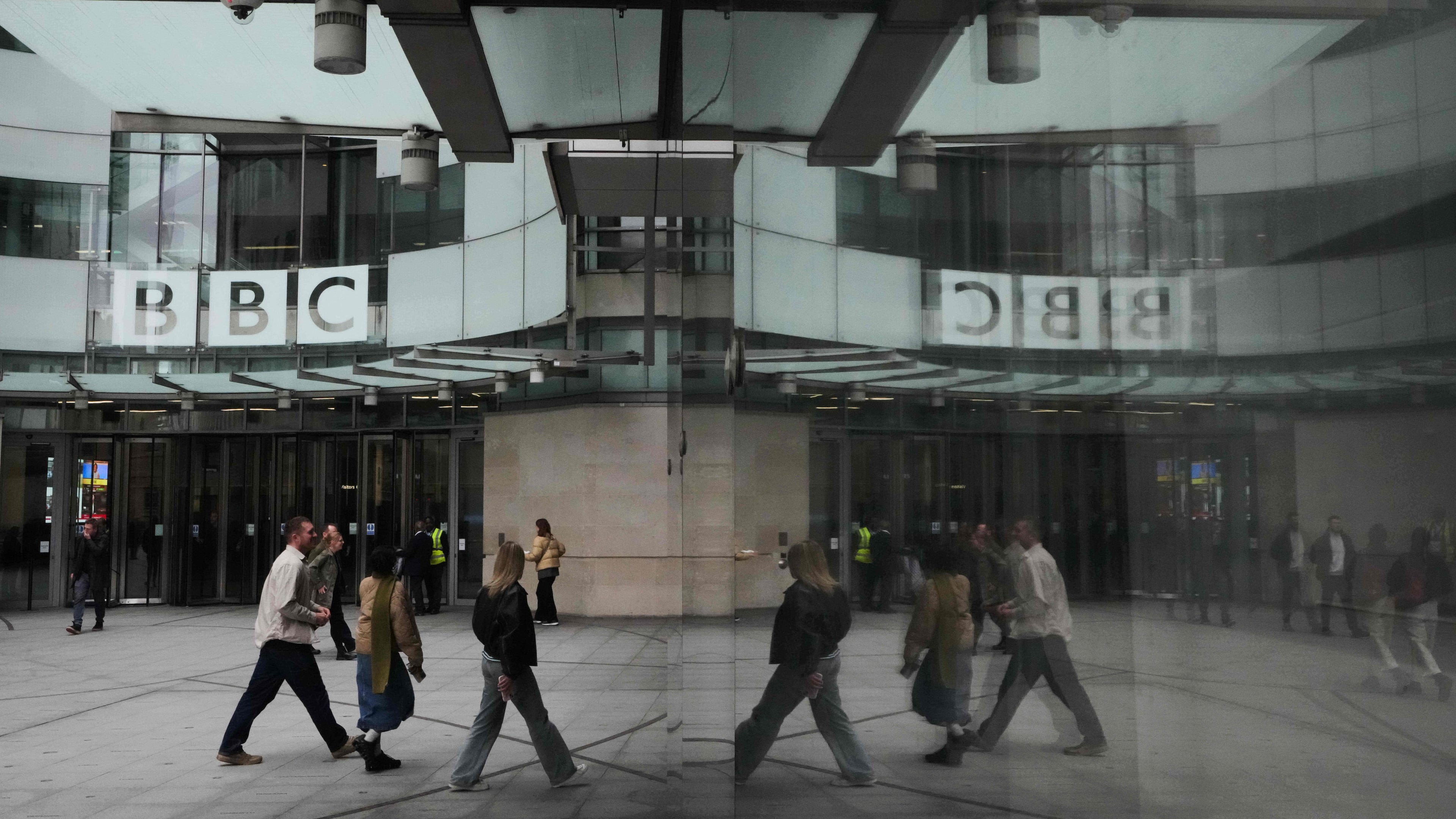 Pedestrians are reflected as they walk outside BBC Broadcasting House in London, Tuesday, Nov. 11, 2025. (AP Photo/Kirsty Wigglesworth)