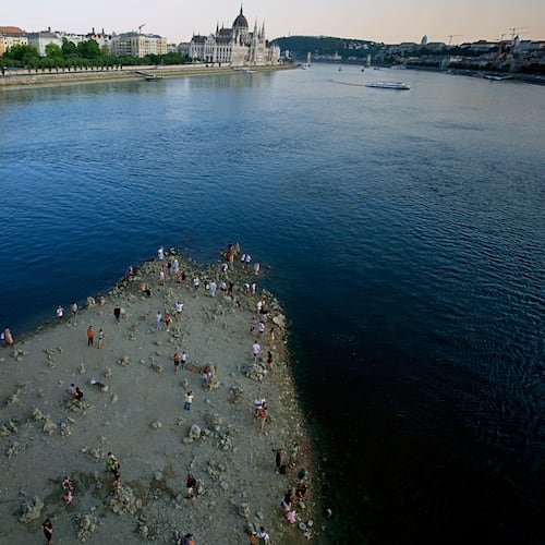 People walk on a sandbar underneath the Danube's Margareth Bridge in downtown Budapest, Hungary, Wednesday Aug. 5, 2026, as the river, which runs through 10 European countries, has receded never-before-seen low water levels. (AP Photo/Bela Szandelszky)