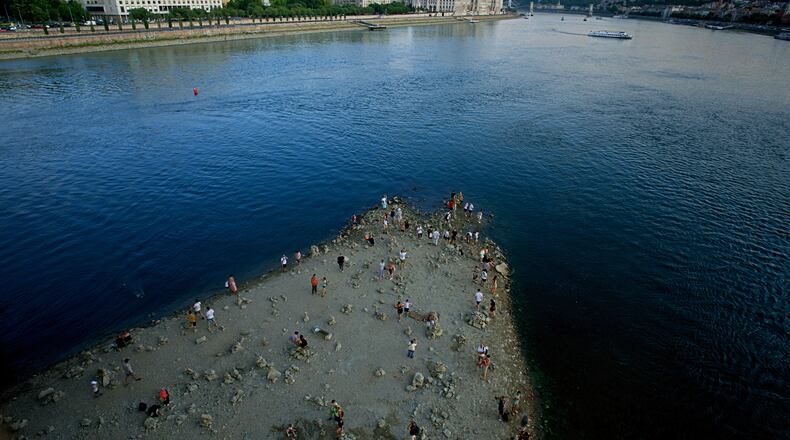 People walk on a sandbar underneath the Danube's Margareth Bridge in downtown Budapest, Hungary, Wednesday Aug. 5, 2026, as the river, which runs through 10 European countries, has receded never-before-seen low water levels. (AP Photo/Bela Szandelszky)
