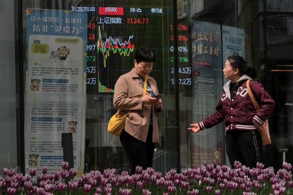 Women talk near an electronic board displaying Shanghai shares trading index at a brokerage house, in Beijing, Tuesday, April 8, 2025. (AP Photo/Andy Wong)