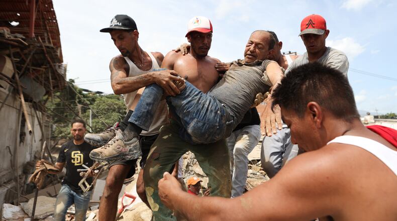 Neighbors carry a man rescued from the rubble of a collapsed building the day after earthquakes struck La Guaira, Venezuela, Thursday, June 25, 2026. (AP Photo/Pedro Mattey)