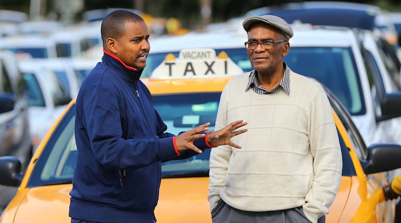 Claude Mayfield (right), 75, who has been a cab driver for more than 30 years at Hartsfield-Jackson International, chats with driver Sharmarke Yonis in the cab holding area. Cab services say they're being hurt by new arrivals such as ride-sharing service Uber and national chain SuperShuttle.