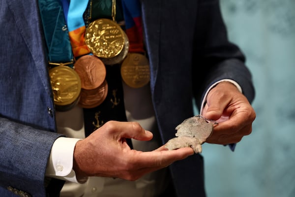 American swimmer Gary Hall Jr. holds an original medal, that melted during the wildfires in Los Angeles that destroyed his home earlier this year, while wearing the replica Olympic medals that IOC President Thomas Bach presented to him during a ceremony at the Olympic House in Lausanne, Switzerland, Monday, May 5, 2025. (Denis Balibouse/Keystone/Reuters Pool via AP)