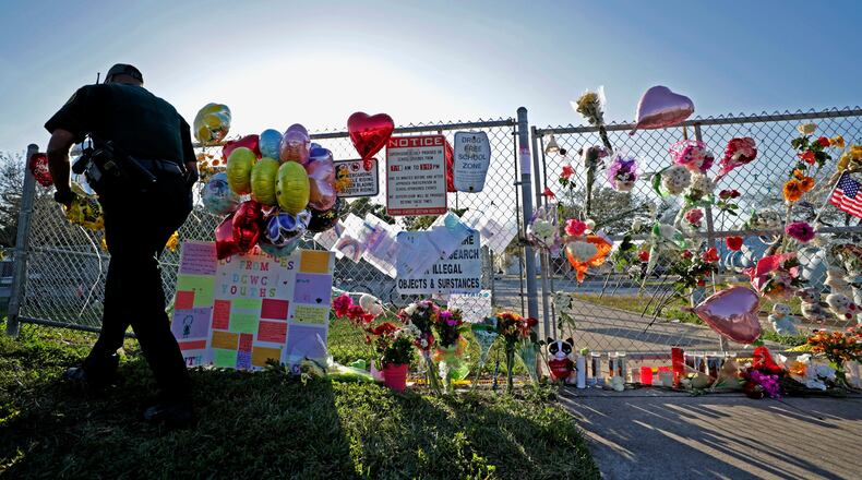 A Broward County Sheriff's Office deputy removes police tape from a makeshift memorial at Marjory Stoneman Douglas High School in Parkland, Fla., Sunday, Feb. 18, 2018. Nikolas Cruz, a former student, was charged with 17 counts of premeditated murder on Thursday. (John McCall/South Florida Sun-Sentinel via AP)