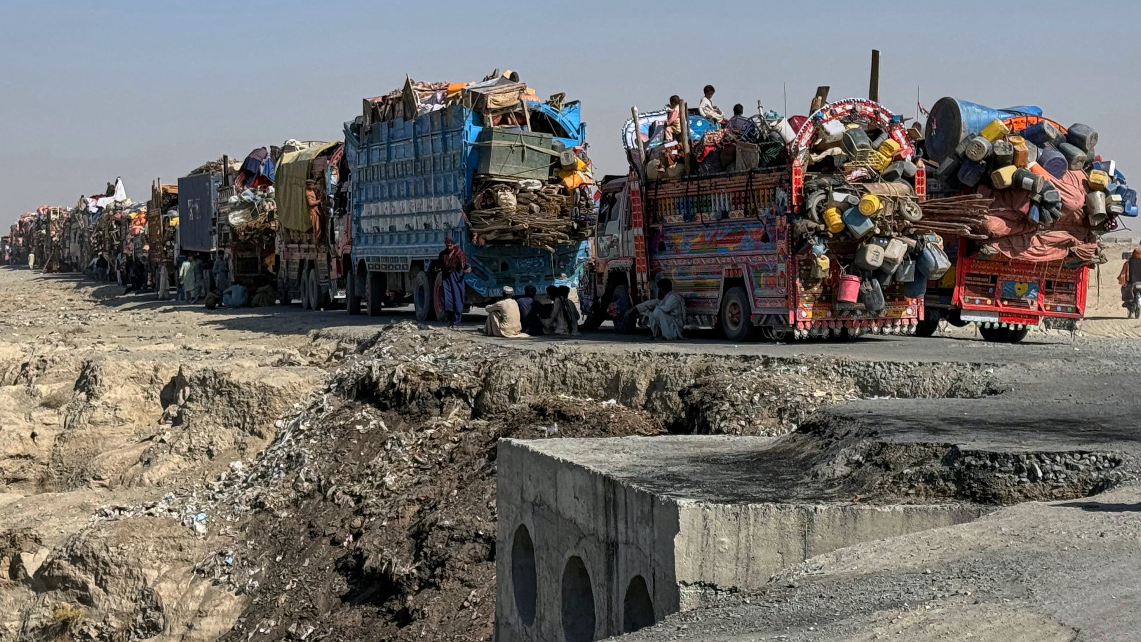 Afghan refugees sit beside trucks loaded with their belongings as they wait their turn to leave for their homeland through a border crossing point which partially opens following Oct.19 ceasefire, on the outskirts of Chaman, a border town on the Pakistan Afghan border, Wednesday, Oct. 29, 2025. (AP Photo/H. Achakzai)