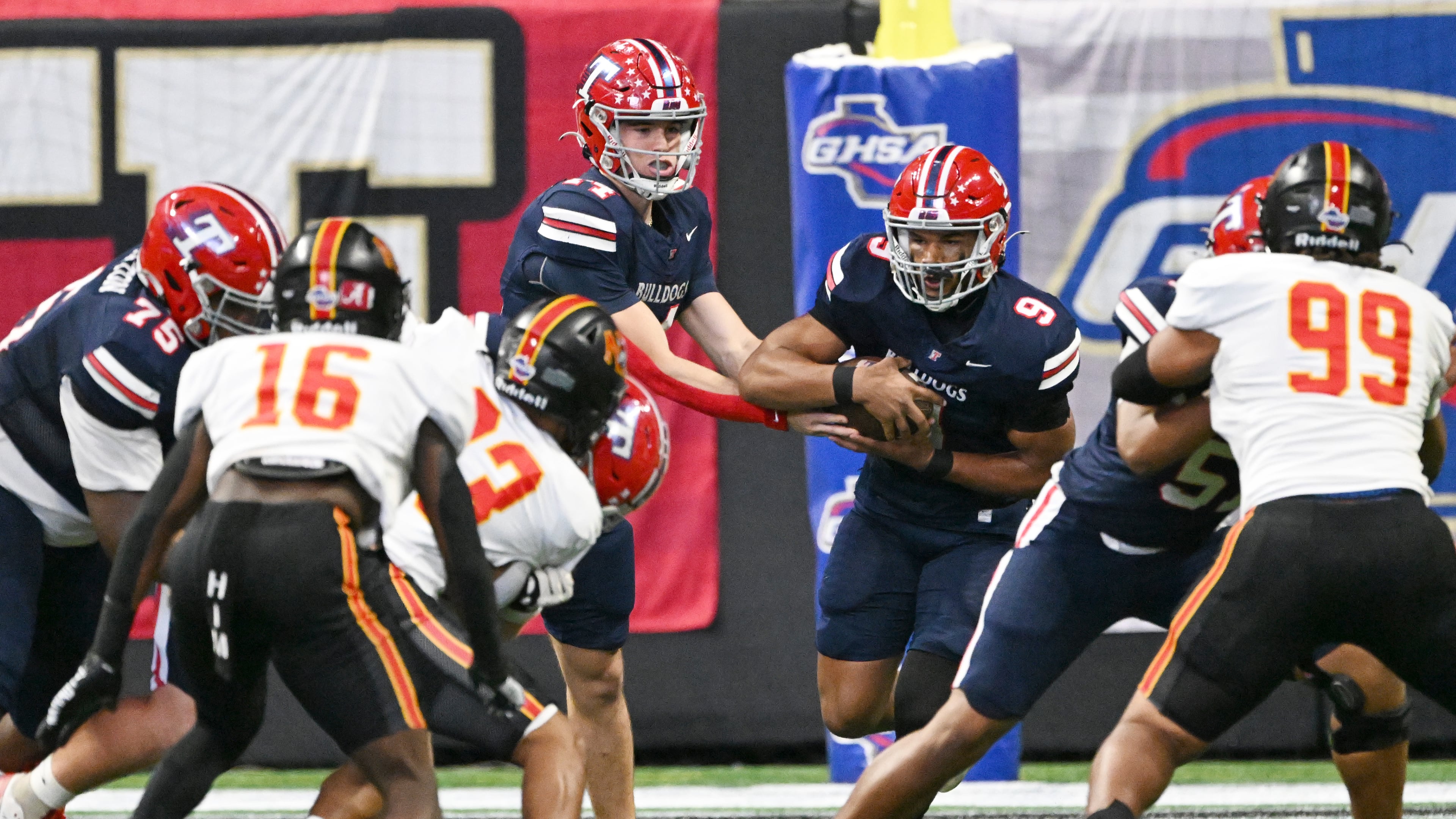 Toombs County's quarterback TJ Stanley (center) makes a handoff to running back Justin Powell during the GHSA Class A Division state championship game at Mercedes-Benz Stadium on Tuesday, Dec. 17, 2024, in Atlanta. Toombs County faces Worth County for the first time next week. (Hyosub Shin/AJC 2024)