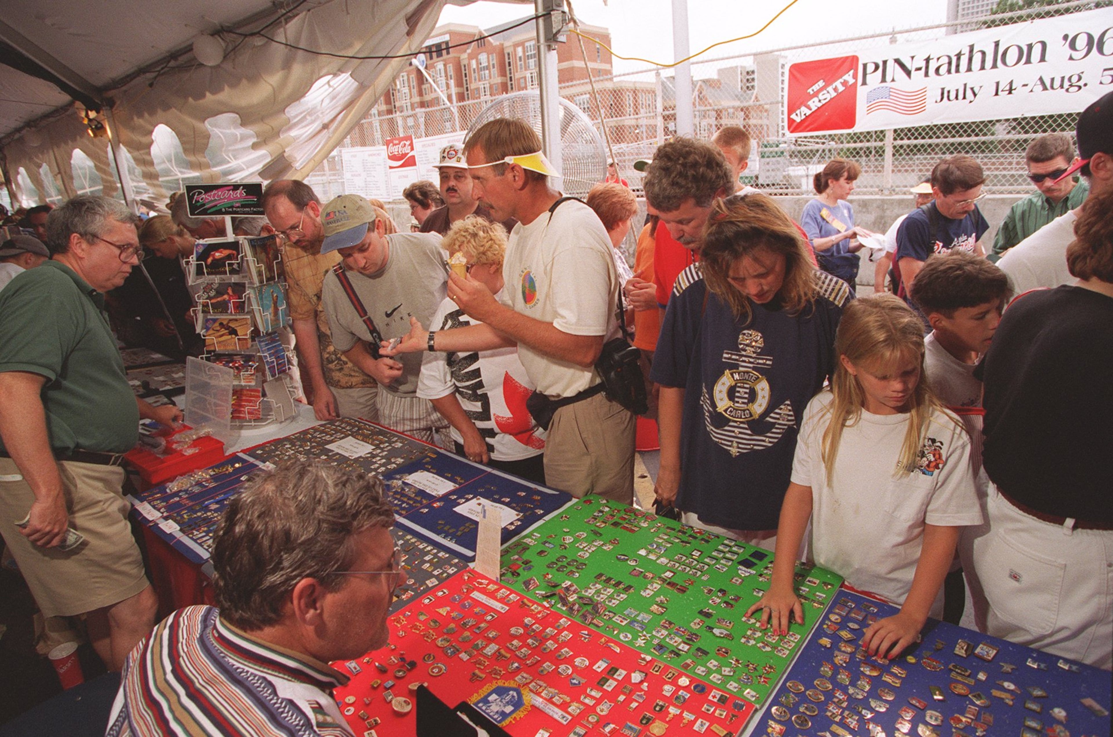 Pin traders look over goods in a tent at the downtown Atlanta location of the Varsity restaurant during the 1996 Summer Olympic Games in Atlanta, Georgia. A feud between the city and street vendors before the start of the Games ended with a court victory in favor of the businesses. (Rich Mahan/AJC 1996)