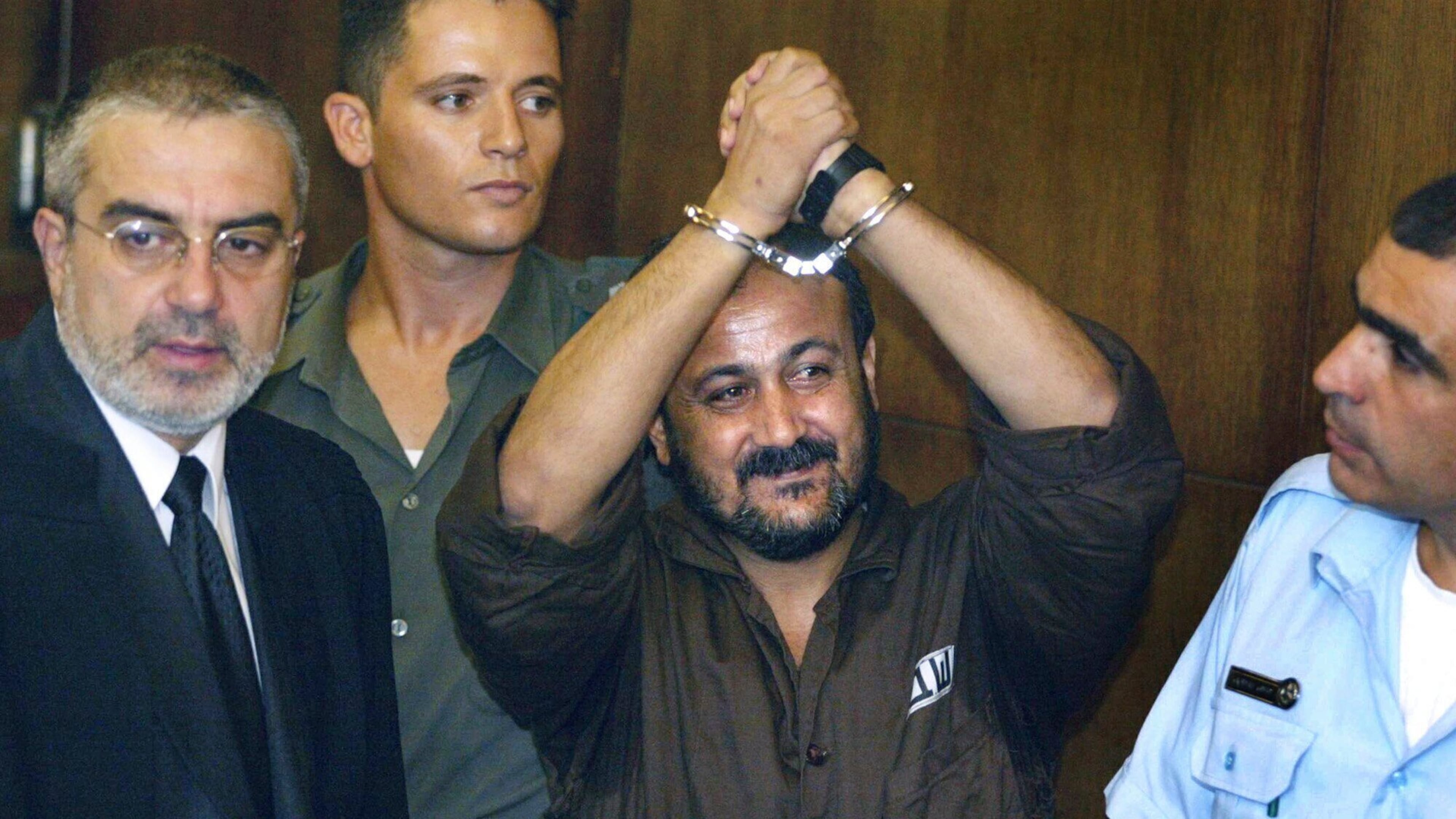 FILE - Marwan Barghouti, center, raises his handcuffed hands in the air on the opening day of his trial in Tel Aviv, Israel, Aug. 14, 2002. (AP Photo/Brennan Linsley, File)