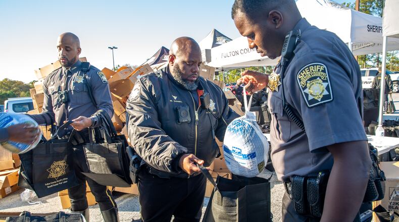 The Fulton County Sheriff's Office gave away about 600 turkeys on Monday at the Old National Discount Mall in College Park. Sgt. Mychal Ammons (from left), Sgt. Markquell Daniel and Deputy Kendrick Sims packaged the turkeys as they came off the truck.