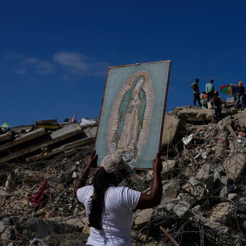 A woman holds a painting of the Virgin Mary as she accompanies a Catholic priest supporting people searching for the remains of relatives in the rubble of residential buildings that collapsed during the earthquakes that struck La Guaira, Venezuela, Friday, July 17, 2026. (AP Photo/Ariana Cubillos)