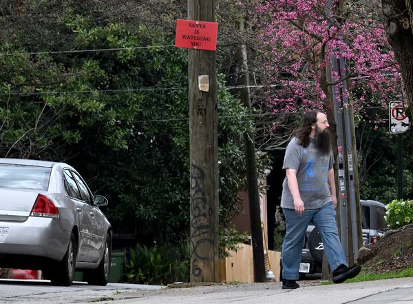 A pedestrian walks past one of the SANTA signs tacked on a pole near Buddy’s convenience store on North Avenue. (Hyosub Shin/AJC)