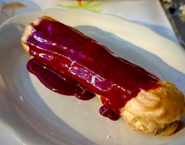 A long, homemade eclair on a plate is topped with a vivid purple sauce made with blackberries.