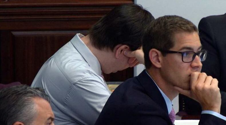 Defendant Ross Harris averts his eyes as the prosecution projected photos of his son’s body onto a large screen in the courtroom. On the right is defense attorney Carlos Rodriguez. Lead defense attorney Maddox Kilgore is at lower left. (Screen capture from WSB-TV video)