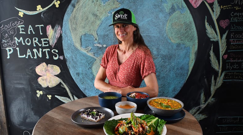Claudine Molson-Sellers, owner and head chef of Strive Foods in Sandy Springs, is shown with several of her dishes: Blueberry Lemon Cheesecake (left), Enchilada Lasagna Burger (front center) and Mango-Zpacho (right). The three condiments are (rear, from left in bowls) Avocado Tomatillo Salsa, Chipotle Mayo, and Pico de Gallo. (Styling by Claudine Molson-Sellers / Chris Hunt for the AJC)