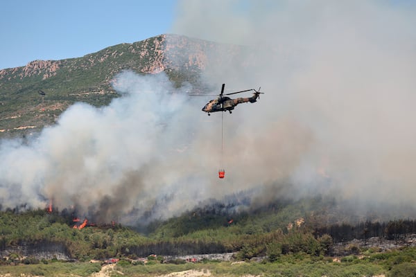 A helicopter sprays water to extinguish a fire in Seferihisar, near Izmir, Turkey, Monday, June 30, 2025. (Cengiz Malgir/Dia Photo via AP)