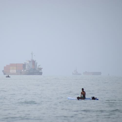 FILE - A man sits on a surfboard as a container ship and other commercial vessels appear anchored in the Strait of Hormuz off Bandar Abbas, Iran, Monday, July 27, 2026. (Razieh Poudat/ISNA via AP, File)