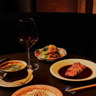 A selection of dishes, including a sliced filet mignon and three vegetable sides, sit on a table in a dark, moody room with a glass of wine