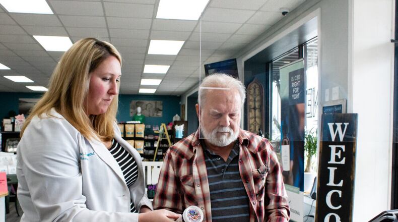 white woman standing on the left, holding pill bottles helping a white man standing to the right