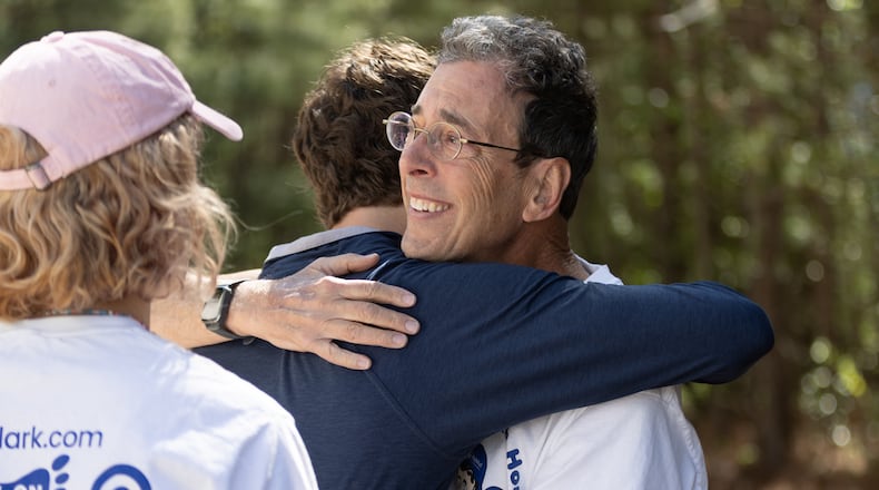Clark Howard gets a hug from his son Grant Howard before the start of the Atlanta Habitat for Humanity dedication of the 98, 99, and 100th Howard's sponsored homes in Atlanta on Saturday, April 13, 2024.  (Steve Schaefer/steve.schaefer@ajc.com)