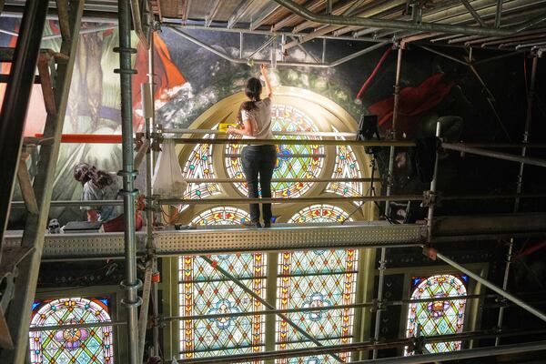 Standing on a 32-foot-tall scaffold, conservation technician Celeste Parrendo works on touching up a mural by Maxo Vanka inside St. Nicholas Croatian Catholic Church in Millvale, Pa., Monday, May 19, 2025. (AP Photo/Gene J. Puskar)