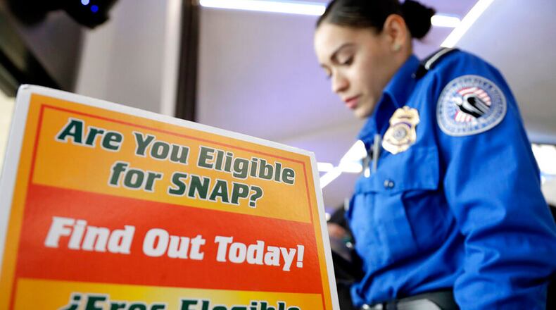 A Transportation Security Administration employee stands at a booth to learn about a food stamp program at a food drive at Newark Liberty International Airport, Wednesday, Jan. 23, 2019, in Newark, N.J. TSA employees each received a box of non perishables and a bag of produce to help them during the shutdown.