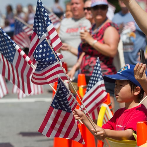 Katsuhiro Watanabe waves four American flags as the Marietta Freedom Parade makes its way down Roswell Street on Tuesday, July 4, 2016, in Marietta, Ga. (Steve Schaefer for the AJC)