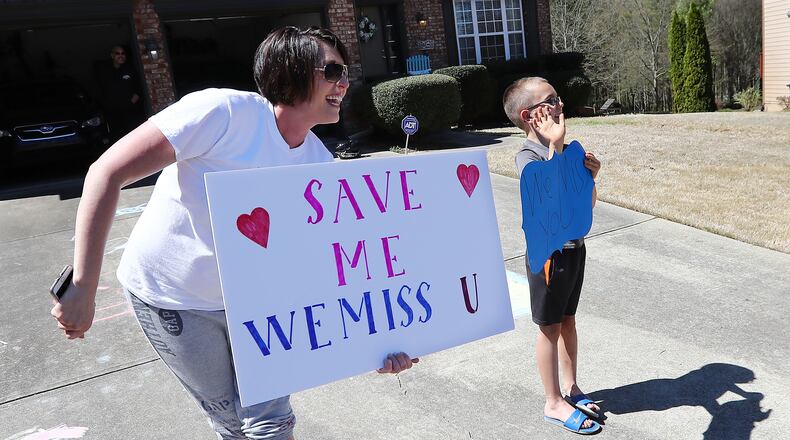 Kelly Osborn and her first grade son Chase, 7, cheer from their driveway as teachers from Roberts Elementary pass by holding an inspirational school parade driving through nearly two dozen area neighborhoods for some face-to-face contact while still maintaining social distance to ease the separation anxiety of their students during the coronavirus on Wednesday, March 25, 2020, in Suwanee. Although distance learning is allowing kids to connect with teachers and get lessons done, the personal touch is missing.