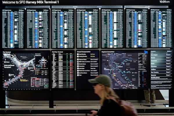 A traveler walks past screens showing outgoing and incoming flights at San Francisco International Airport ahead of the Memorial Day holiday weekend in San Francisco, Thursday, May 22, 2025. (AP Photo/Godofredo A. Vásquez)