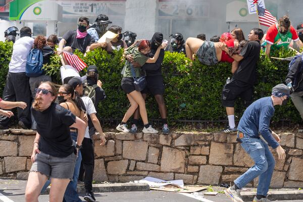 Demonstrators climb a hedge to avoid tear gas during a protest on ICE raids and deportation arrests on Chamblee Tucker Road in Atlanta on Saturday, June 14, 2025. (Arvin Temkar/AJC)