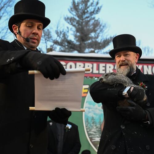 Groundhog Club Vice President Dan McGinley reads the scroll as handler A.J. Dereume holds Punxsutawney Phil, the weather prognosticating groundhog, during the 140th celebration of Groundhog Day on Gobbler's Knob in Punxsutawney, Pa., Monday, Feb. 2, 2026, Phil's handlers said that the groundhog has forecast six more weeks of winter. (AP Photo/Barry Reeger)