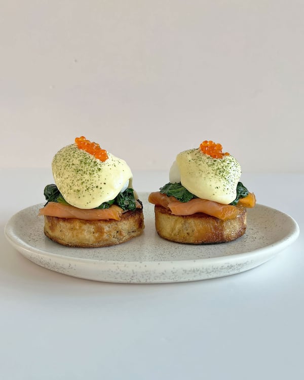 Two English muffins sit on a white plate, topped with smoked salmon, an egg and Hollandaise sauce.