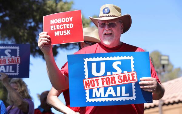 FILE - Letter carrier Fred Moss holds up signs during a protest, part of a national series of rallies against the Trump administration's plans to privatize or restructure the U.S. Postal Service, Sunday, March 23, 2025, in Las Vegas. (Steve Marcus/Las Vegas Sun via AP, File)