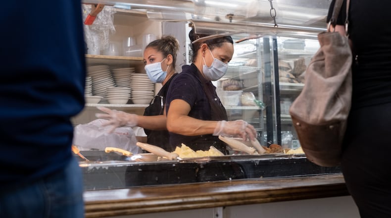 Ingred Cruez (left) and Marie Rodriguez help customers from behind acrylic panels during the lunch rush at Matthews Cafeteria on Main Street in Tucker.  Ben Gray for The Atlanta Journal-Constitution