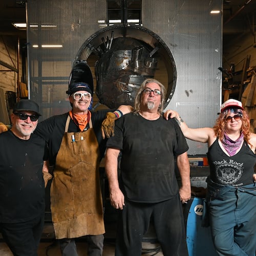 Charlie “Blackcat” Smith (third from left) poses with other artists who've worked on "The Burning Book" sculpture for Burning Man: (from left) Michael Marlingde Cuellar, Jeffery “PAPR” Morgan and Cloe Ashton. The sculpture (seen in the background) will appear at the annual Burning Man festival in Nevada’s Black Rock Desert. (Hyosub Shin/AJC)