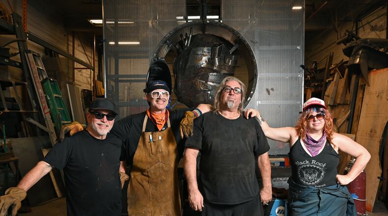 Charlie “Blackcat” Smith (third from left) poses with other artists who've worked on "The Burning Book" sculpture for Burning Man: (from left) Michael Marlingde Cuellar, Jeffery “PAPR” Morgan and Cloe Ashton. The sculpture (seen in the background) will appear at the annual Burning Man festival in Nevada’s Black Rock Desert. (Hyosub Shin/AJC)