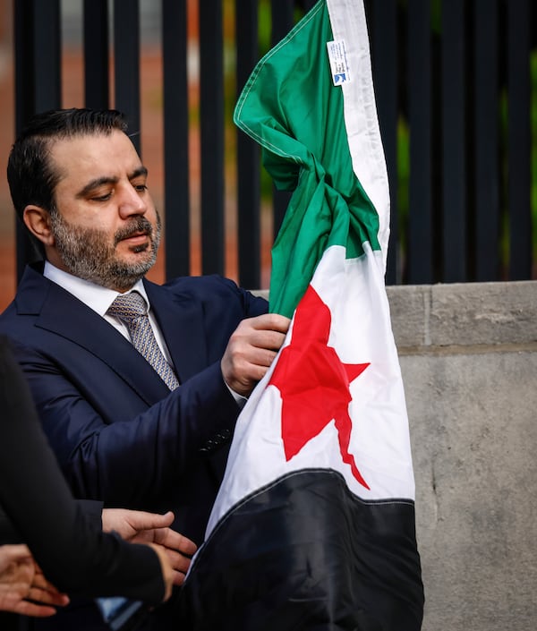 Syria's Foreign Minister Asaad Al-Shibani unfolds the Syrian Flag during a ceremony where the Syrian flag was added to the 100 flags flying in line at United Nations Headquarters on Friday, April 25, 2025. (AP Photo/Kena Betancur)