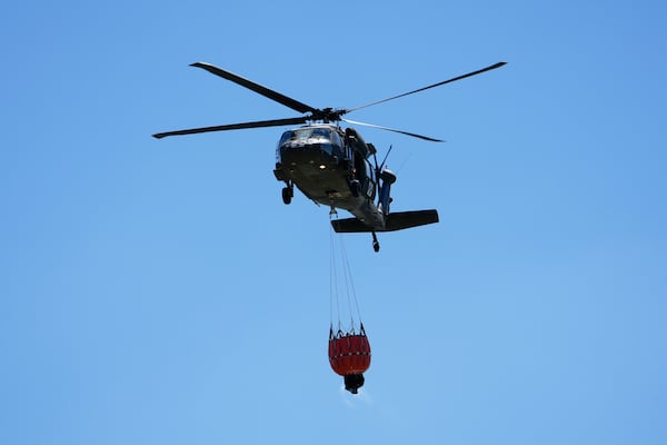 A helicopter carries water to battle the Pauline Road wildfire Thursday, March 20, 2025, in Cleveland, Texas. (AP Photo/David J. Phillip)