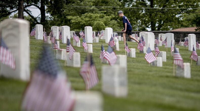 American flags are seen in front of headstones as a young boy walks through Marietta National Cemetery on Saturday, May 26, 2018, ahead of Memorial Day. Boy Scouts along with help from Girl Scouts, Brownies and Daisies ensure the flags are placed properly. BRANDEN CAMP / CONTRIBUTED