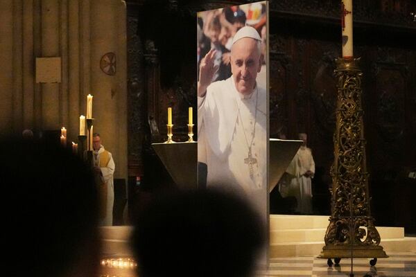 People attend a ceremony inside Notre Dame cathedral where a poster shows Pope Francis following the Vatican's announcement of his death, Monday, April 21, 2025 in Paris. (AP Photo/Thibault Camus)