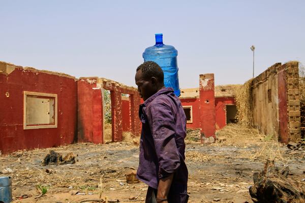 A man carries a water container past a building damaged during the civil war at a distribution point due to water outages in Khartoum, Sudan, Sunday, May 25, 2025. (AP Photo)
