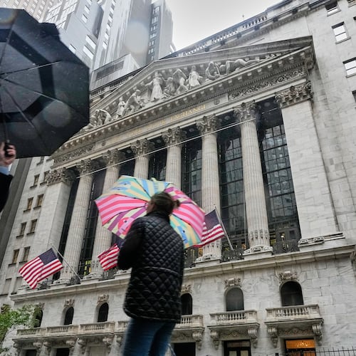 People with umbrellas pass the New York Stock Exchange, Monday, Oct. 13, 2025. (AP Photo/Richard Drew)