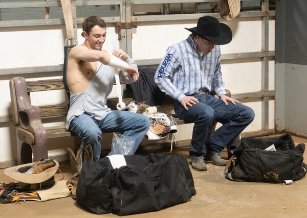 two white men sitting on a bench, left man wrapping his arim and right man with cowboy hat on. 