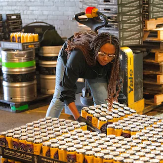 Jossette Footmon-Smith, one of Our Culture Brewing Company's partners, places cases of beer on a pallet for distribution to retail stores.
