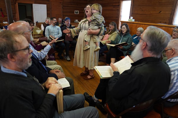 Sarah George, who met her husband through Sacred Harp singing, holds their son while leading a song from the hollow square at a Sacred Harp gathering in Bremen, Ga., at Holly Springs Primitive Baptist Church on Saturday, March 22, 2025. (AP Photo/Jessie Wardarski)